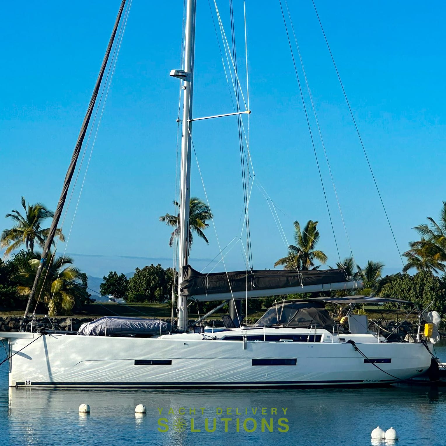 A white dufour 56 tied to the dock in Vuda Marina after the yacht delivery skipper finished the trip to Fiji. the boat is white, the sky is blue and the water is flat and blue