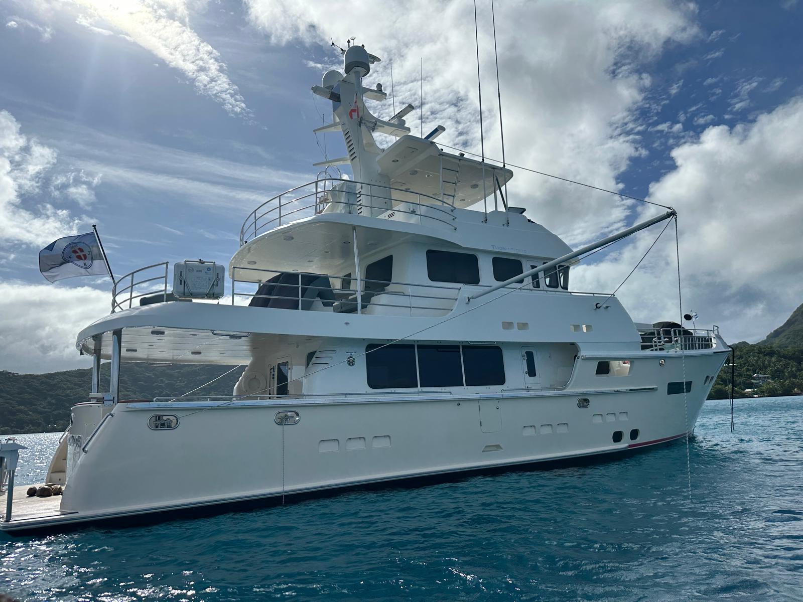 Nordhavn 76 that's cream colour anchored in Bora Bora in blue water with blue sky. Yacht delivery solutions skipper is taking it to fiji