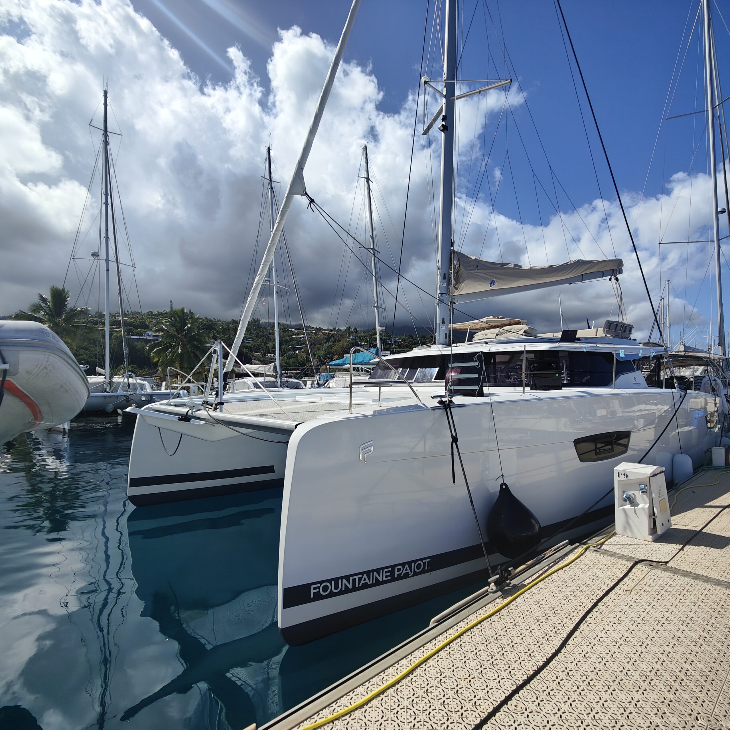 Fountaine Pajot catamaran tied to the dock. the view is from the dock looking to the white bow with a grey stripe and white fluffy clouds with blue sky after a yacht delivery