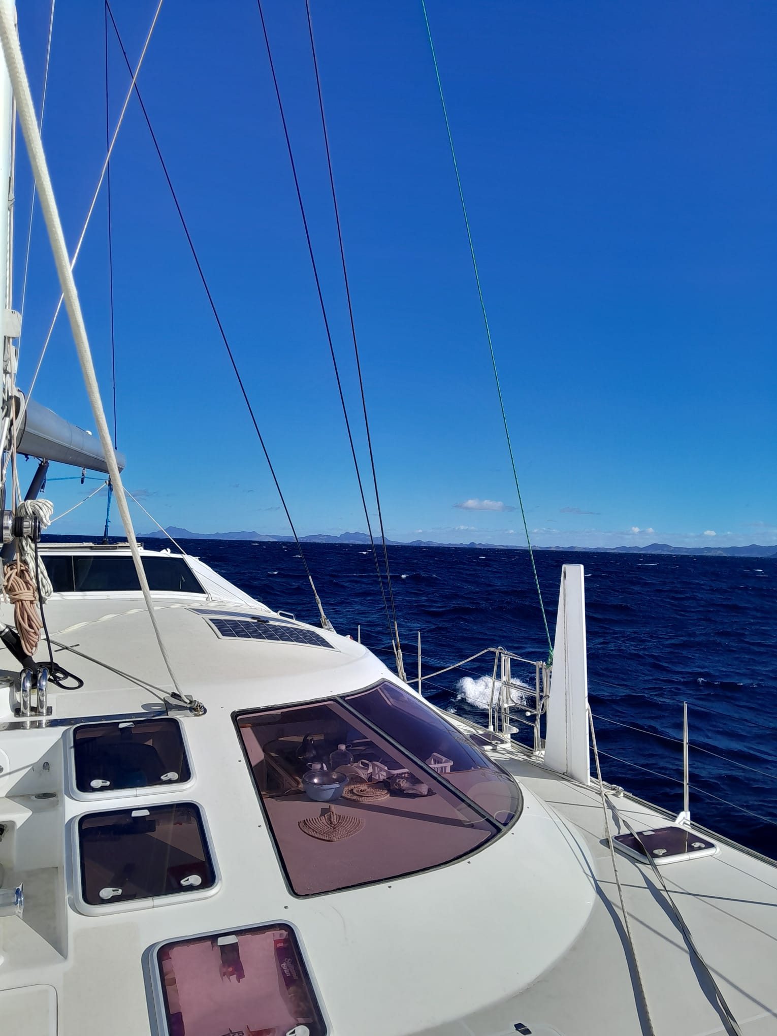 a white Schionning 1600 with a flat sea and blue sky with land in the back ground on a yacht delivery to fiji